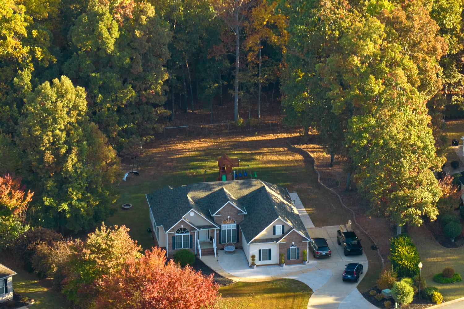 Aerial view of a house surrounded by trees with a driveway and cars.